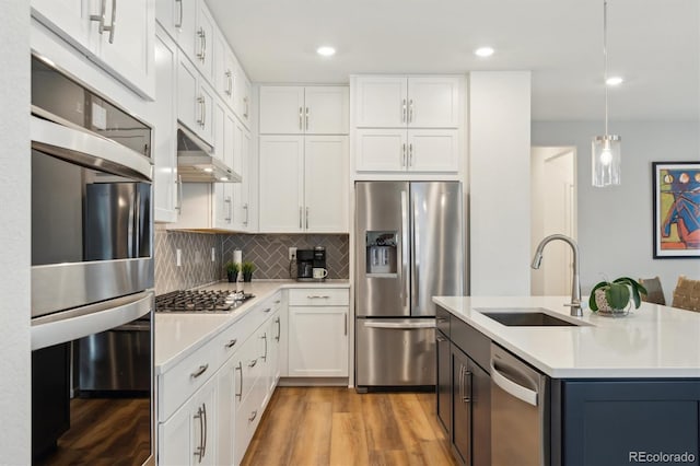 kitchen featuring under cabinet range hood, a sink, light countertops, appliances with stainless steel finishes, and tasteful backsplash