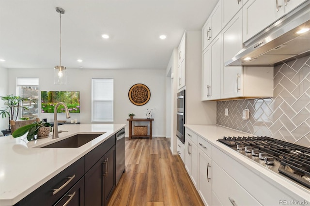 kitchen with white cabinets, stainless steel appliances, light countertops, under cabinet range hood, and a sink