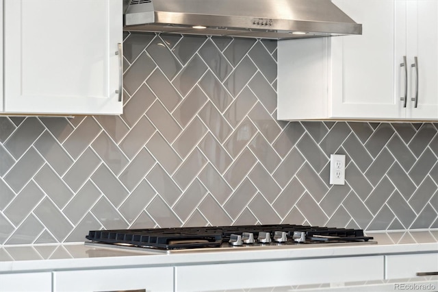 kitchen featuring stainless steel gas stovetop, white cabinetry, decorative backsplash, and exhaust hood