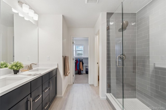 bathroom featuring double vanity, a stall shower, a sink, and wood finished floors