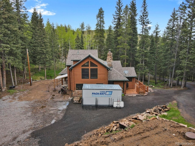 8905 Carol Ln, Conifer, CO 80433 - view of front of house with log siding, a forest view, a chimney, and roof with shingles
