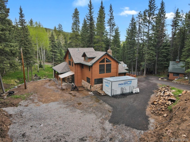 8905 Carol Ln, Conifer, CO 80433 - view of front facade featuring log exterior, a chimney, a view of trees, and a shingled roof