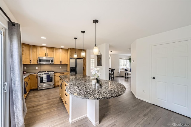 kitchen with wood finished floors, a center island, tasteful backsplash, dark stone countertops, and appliances with stainless steel finishes