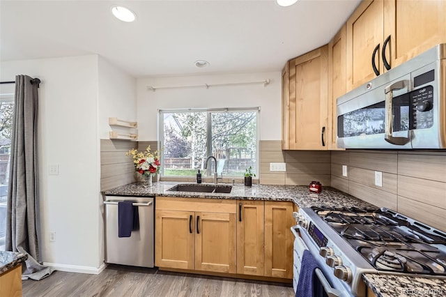 kitchen with a sink, appliances with stainless steel finishes, light wood finished floors, and dark stone countertops