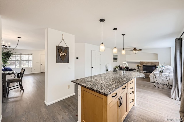 kitchen with a fireplace, ceiling fan with notable chandelier, open floor plan, a kitchen island, and dark wood-style floors
