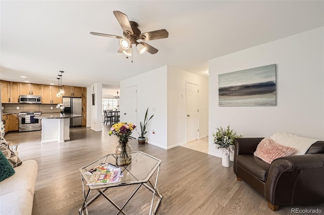 living area featuring baseboards, a ceiling fan, light wood finished floors, and recessed lighting