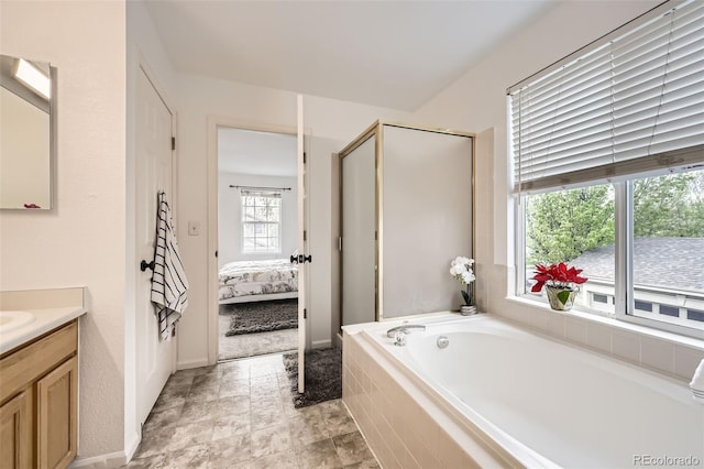 bathroom with a garden tub, a stall shower, vanity, baseboards, and ensuite bath
