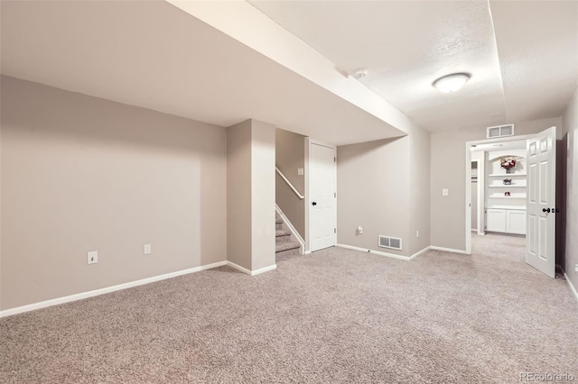 finished below grade area featuring visible vents, baseboards, stairs, and light carpet