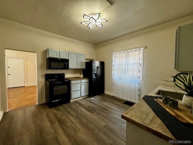 kitchen with a textured ceiling, dark wood-type flooring, and black appliances