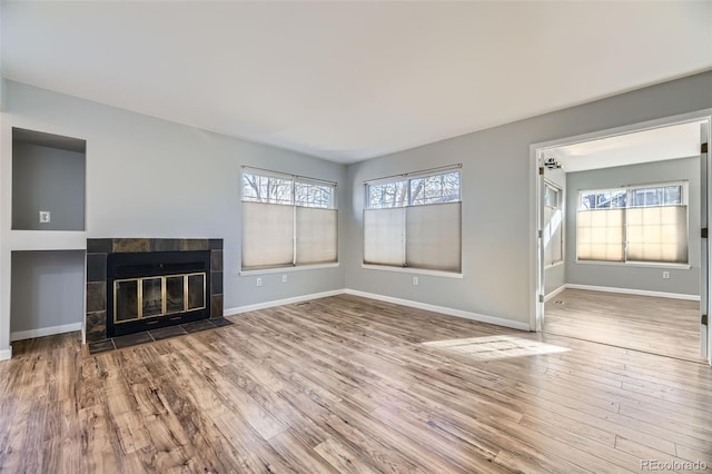 unfurnished living room featuring a tiled fireplace, hardwood / wood-style floors, and a wealth of natural light