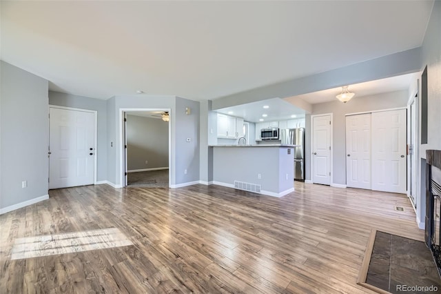 unfurnished living room featuring hardwood / wood-style floors, sink, and ceiling fan