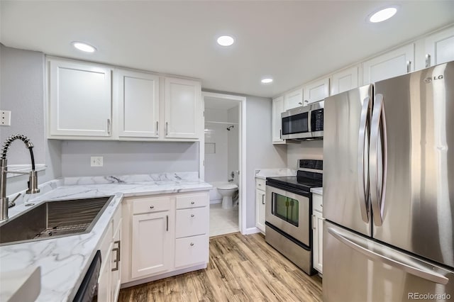 kitchen with white cabinetry, appliances with stainless steel finishes, sink, and light stone counters