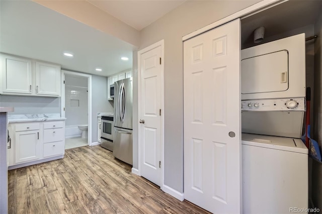 kitchen with light hardwood / wood-style flooring, stainless steel appliances, stacked washer and clothes dryer, and white cabinets