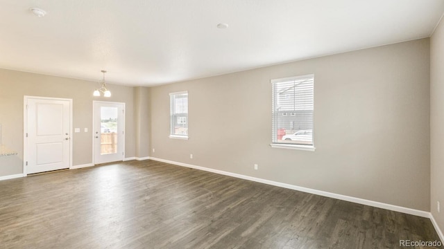 empty room with plenty of natural light, a chandelier, and dark hardwood / wood-style floors