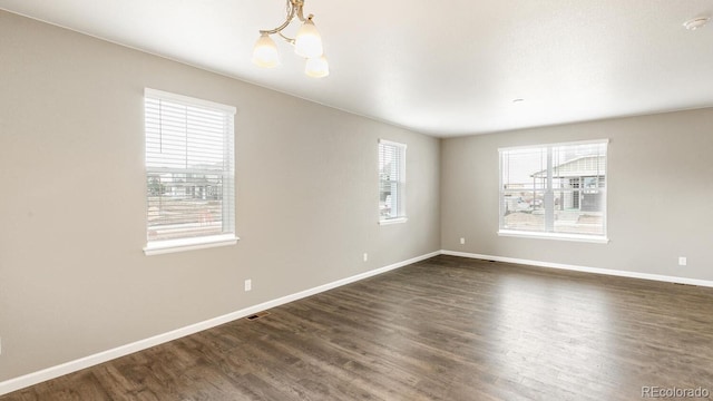 unfurnished room with plenty of natural light, an inviting chandelier, and dark hardwood / wood-style floors