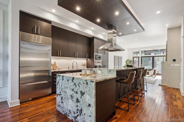 370 Garfield St, Denver, CO 80206 - kitchen with built in appliances, island exhaust hood, dark wood finished floors, decorative backsplash, and a breakfast bar