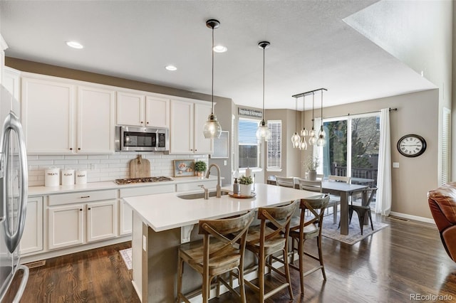 kitchen featuring tasteful backsplash, dark wood finished floors, light countertops, stainless steel appliances, and a sink