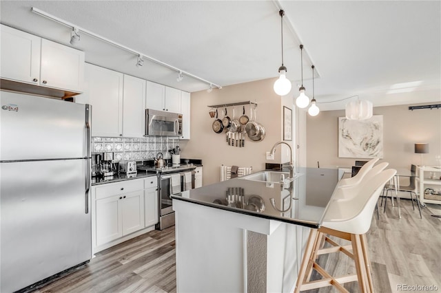 1150 Vine St Unit 201, Denver, CO 80206 - kitchen featuring appliances with stainless steel finishes, a sink, dark countertops, light wood-type flooring, and a kitchen bar