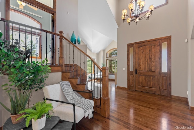 foyer with wood finished floors, a notable chandelier, stairway, baseboards, and a towering ceiling