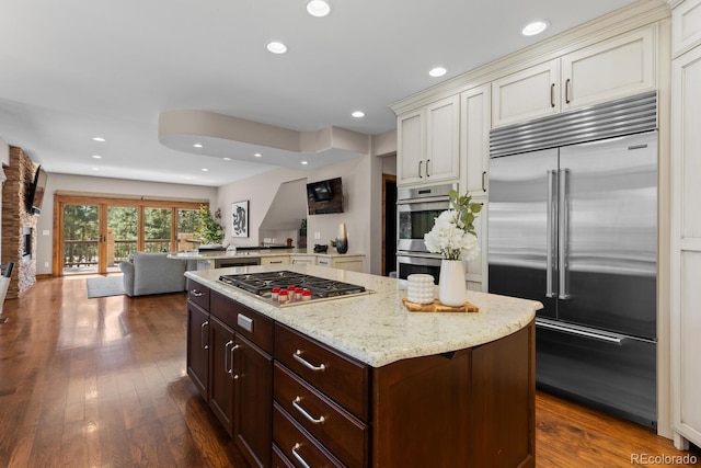 kitchen with dark brown cabinets, recessed lighting, appliances with stainless steel finishes, light stone counters, and dark wood-style floors