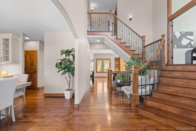 entryway with stairs, wood finished floors, arched walkways, a high ceiling, and baseboards