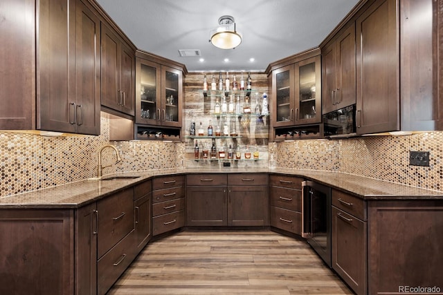 kitchen featuring dark brown cabinets, visible vents, a sink, dark stone counters, and light wood-type flooring