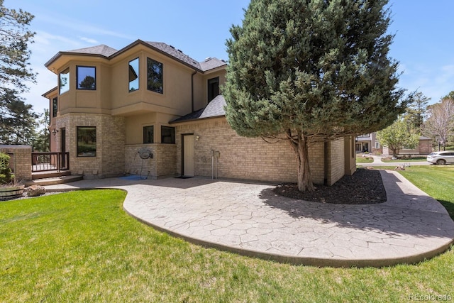 rear view of house with a yard, a patio area, stucco siding, and brick siding