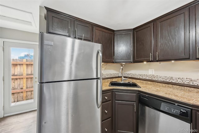 kitchen featuring stainless steel appliances, light stone countertops, sink, and dark brown cabinetry