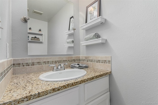 11147 W 17th Ave Unit 103, Lakewood, CO 80215 - bathroom with visible vents, a textured wall, vanity, and tasteful backsplash