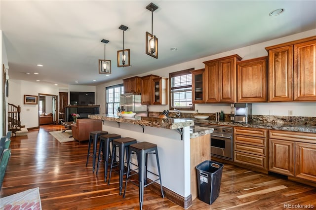690 S Emerson St, Denver, CO 80209 - kitchen featuring appliances with stainless steel finishes, brown cabinets, a kitchen bar, dark wood-style flooring, and recessed lighting