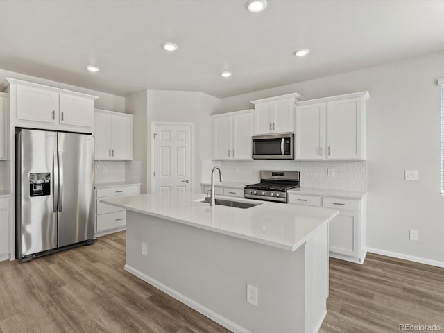 kitchen featuring appliances with stainless steel finishes, a sink, wood finished floors, backsplash, and recessed lighting