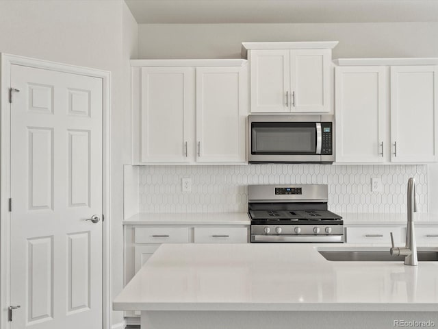 kitchen with stainless steel appliances, a sink, white cabinetry, and backsplash