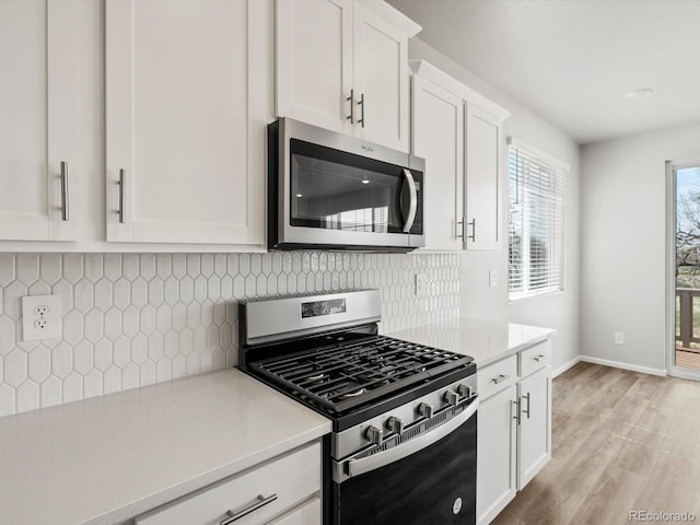 kitchen featuring appliances with stainless steel finishes, light countertops, white cabinetry, light wood-type flooring, and backsplash