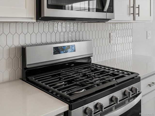 kitchen view of appliances with stainless steel finishes, backsplash, white cabinetry, and light countertops