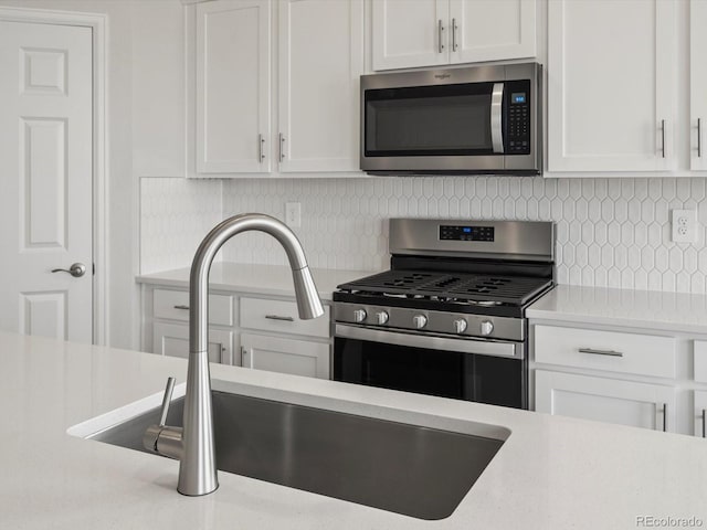 kitchen with stainless steel appliances, a sink, light countertops, white cabinetry, and tasteful backsplash