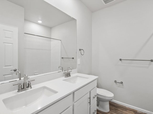 bathroom featuring toilet, baseboards, wood finished floors, double vanity, and a shower