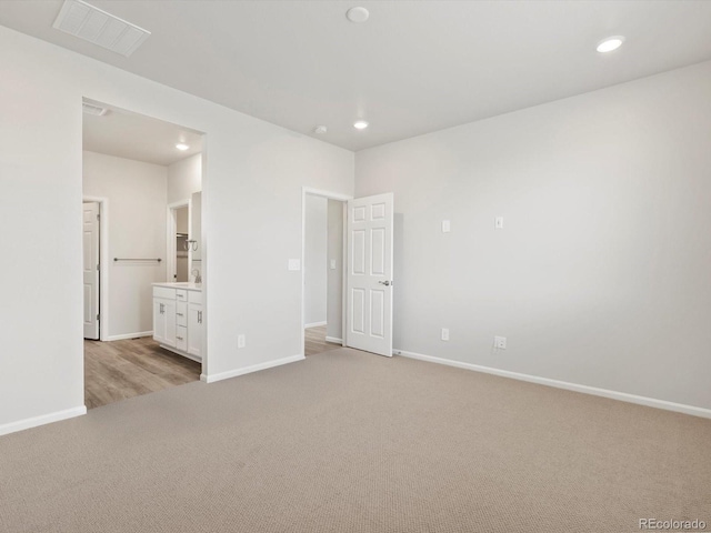 unfurnished bedroom with light colored carpet, baseboards, recessed lighting, and ensuite bath