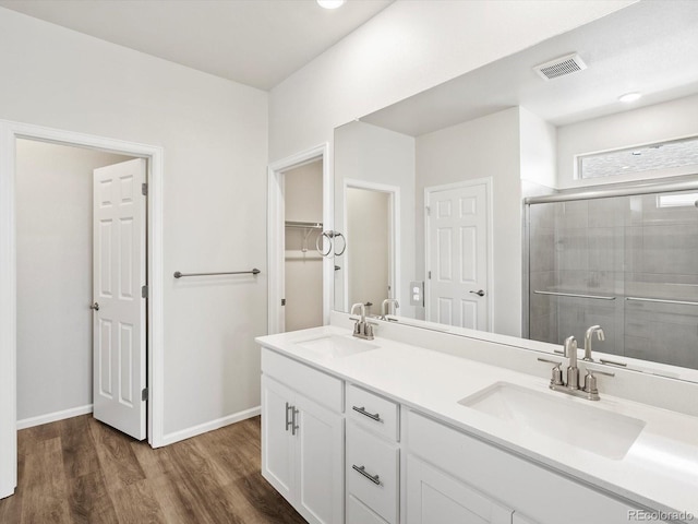 full bath featuring a shower stall, wood finished floors, double vanity, baseboards, and a spacious closet