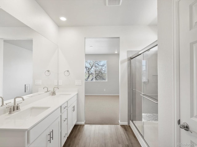 full bath with wood finished floors, baseboards, a stall shower, double vanity, and recessed lighting