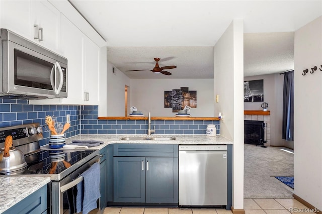 kitchen with blue cabinetry, sink, a tile fireplace, light colored carpet, and stainless steel appliances