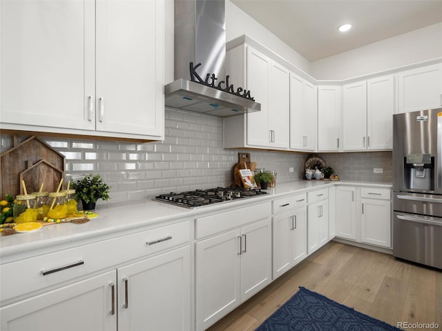 kitchen featuring white cabinets, appliances with stainless steel finishes, light countertops, light wood-type flooring, and wall chimney range hood