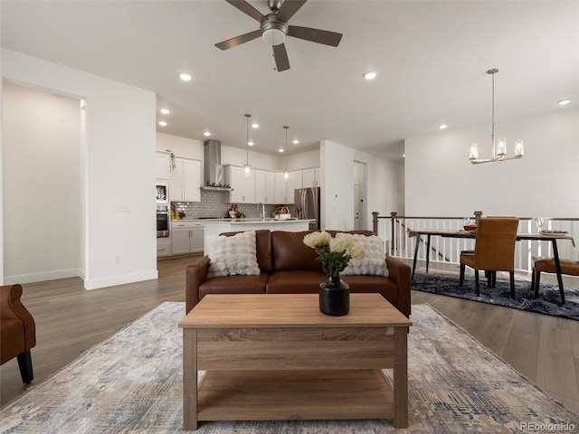 living area with ceiling fan with notable chandelier, baseboards, wood finished floors, and recessed lighting