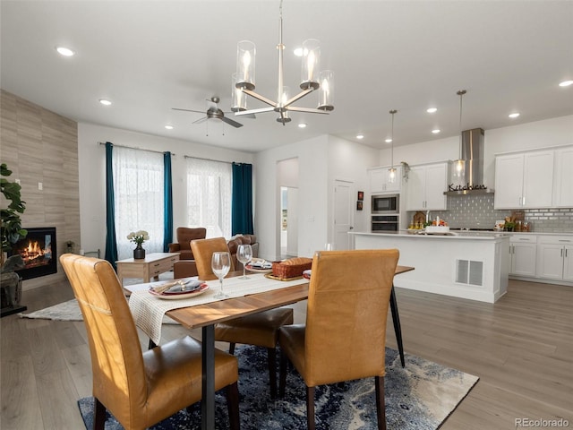 dining area featuring light wood finished floors, visible vents, a tiled fireplace, and recessed lighting