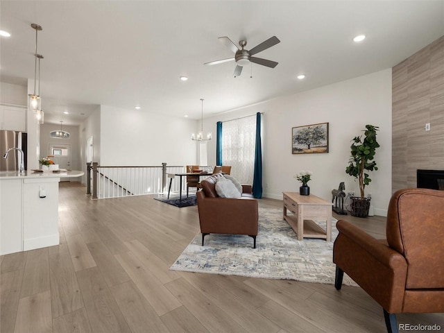 living room featuring recessed lighting, light wood-style flooring, a tiled fireplace, and ceiling fan with notable chandelier