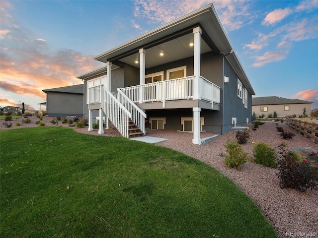 back of house at dusk with stucco siding, a yard, and stairs