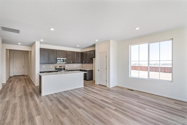 kitchen featuring dark brown cabinetry, sink, stainless steel appliances, an island with sink, and light hardwood / wood-style floors