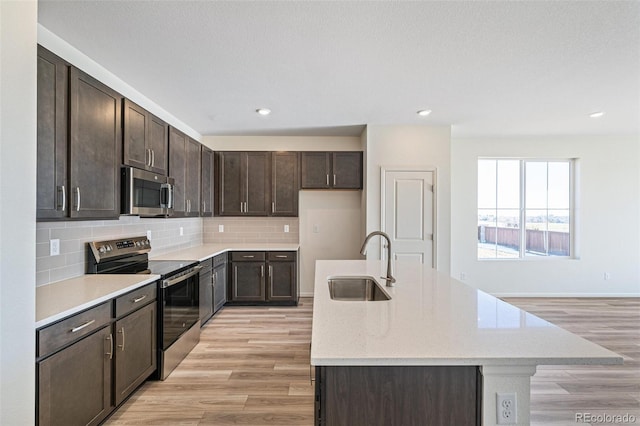 kitchen featuring a kitchen island with sink, sink, tasteful backsplash, light hardwood / wood-style floors, and stainless steel appliances