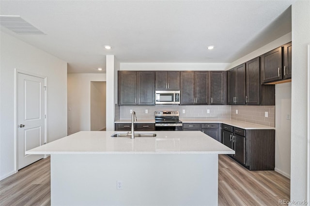 kitchen featuring appliances with stainless steel finishes, a center island with sink, light hardwood / wood-style flooring, and sink