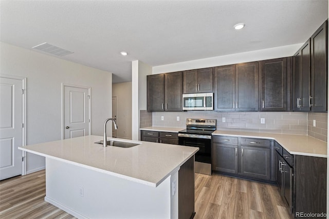 kitchen featuring sink, stainless steel appliances, light hardwood / wood-style flooring, decorative backsplash, and a center island with sink