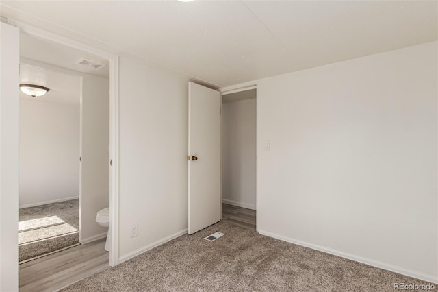 unfurnished bedroom with light wood-type flooring, ensuite bath, and a closet